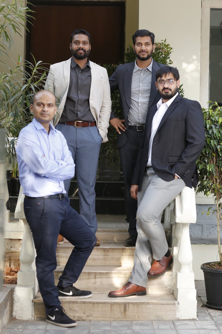 The four Kritsnam co-founders — Prudhvi Sagar, Vinay Chataraju, K. Sri Harsha and a fourth teammate — posed on the steps of the SIIC IIT Kanpur incubator, in a mix of business casual and formal attire, plants and a doorway behind them.