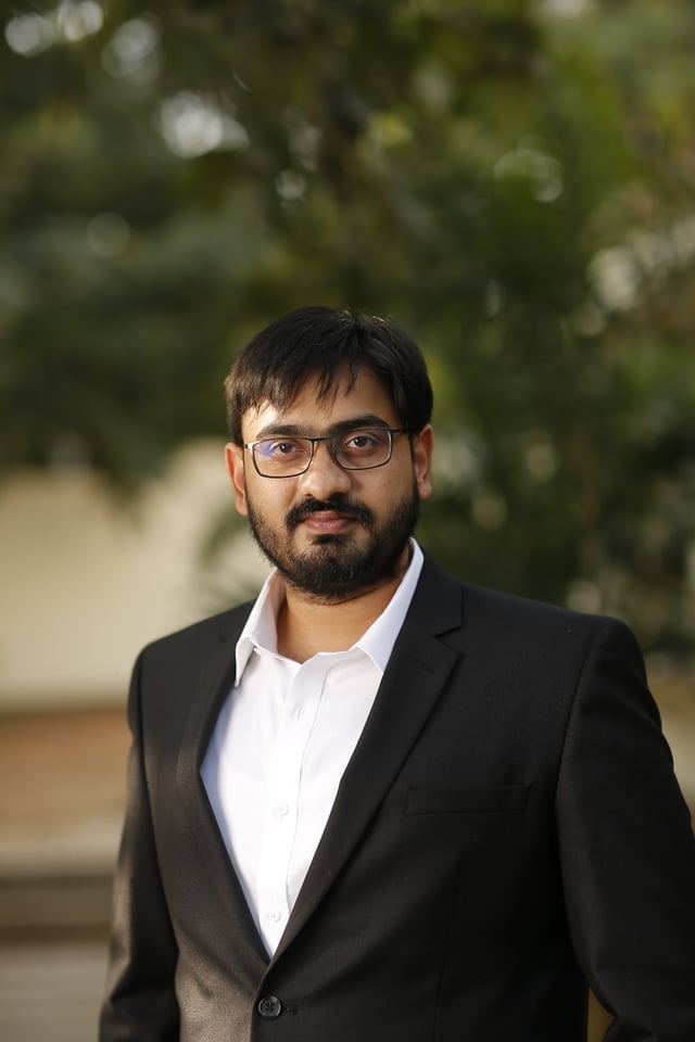 K. Sri Harsha, Founder & Managing Director of Kritsnam Technologies — bearded, wearing glasses, in a black blazer over a white shirt, standing in a doorway with soft natural light behind him.