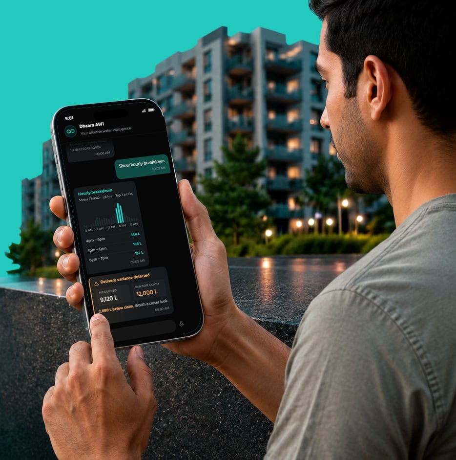 A man in a grey T-shirt reviewing a Dhaara AWI hourly-breakdown dashboard on his phone in front of a modern apartment complex, with a black Dhaara Pulse device beside him at dusk.