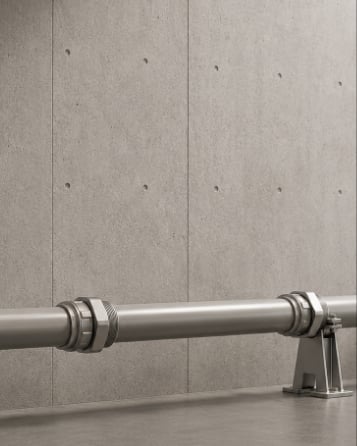A bare metal water pipe running along a concrete wall.